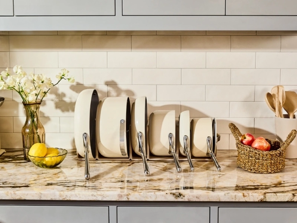 Set of cream-colored pots and pans neatly organized on a marble countertop with flowers and lemons