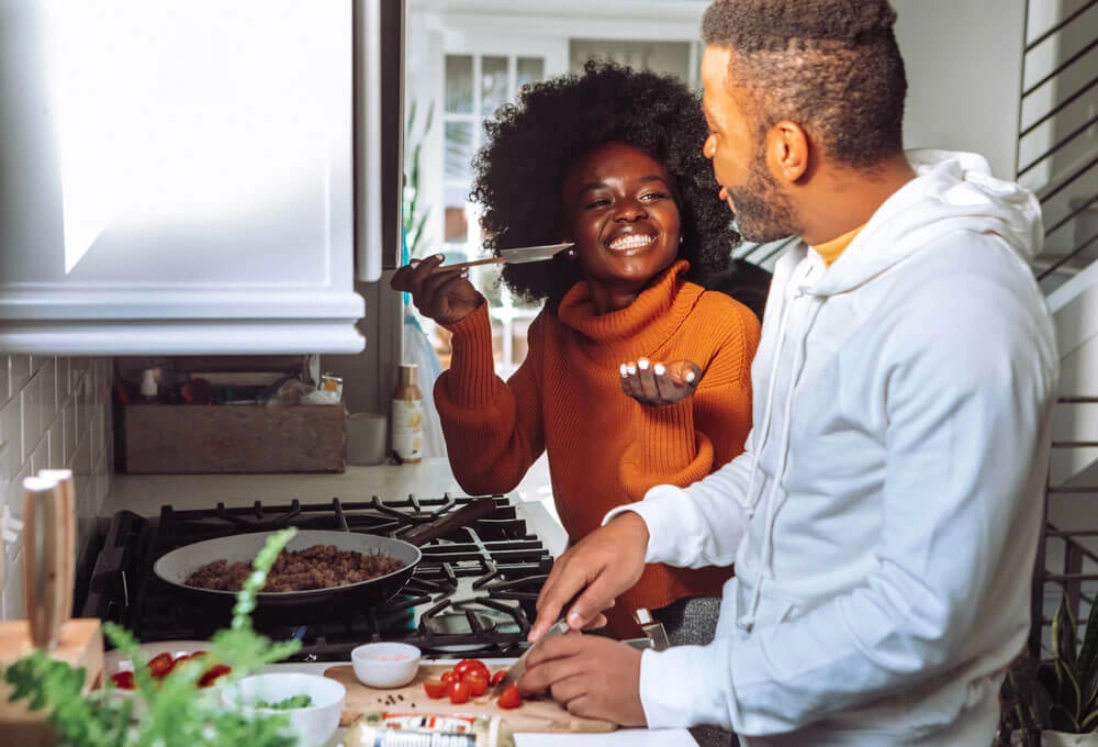 Smiling woman playfully holds a spatula while cooking with a man who is chopping vegetables