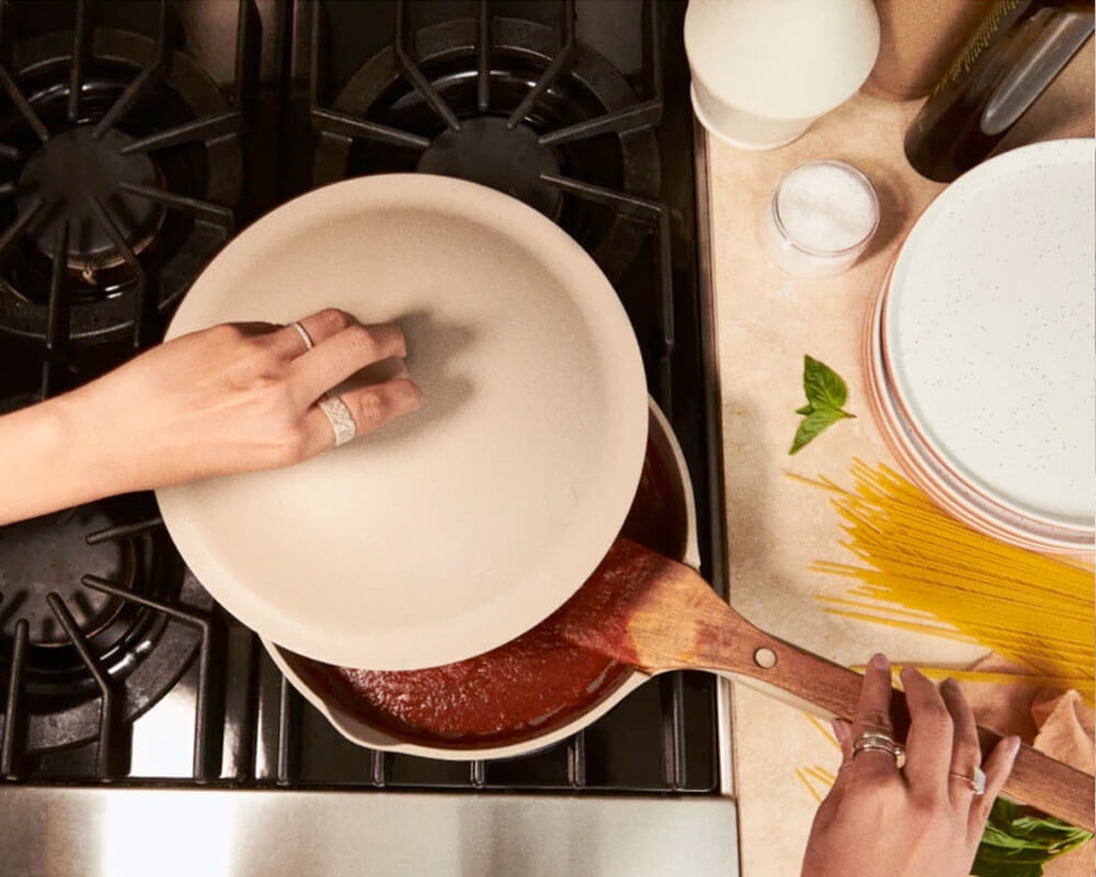 Woman removing the lid from a frying pan in the stovetop