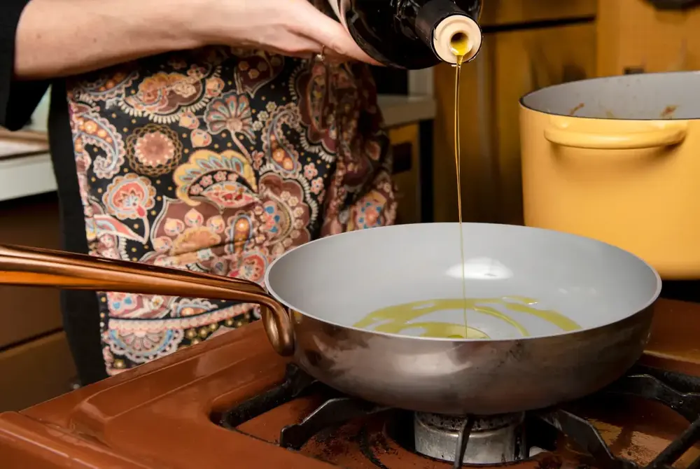 woman cooking in a ceramic frying pan with olive oil