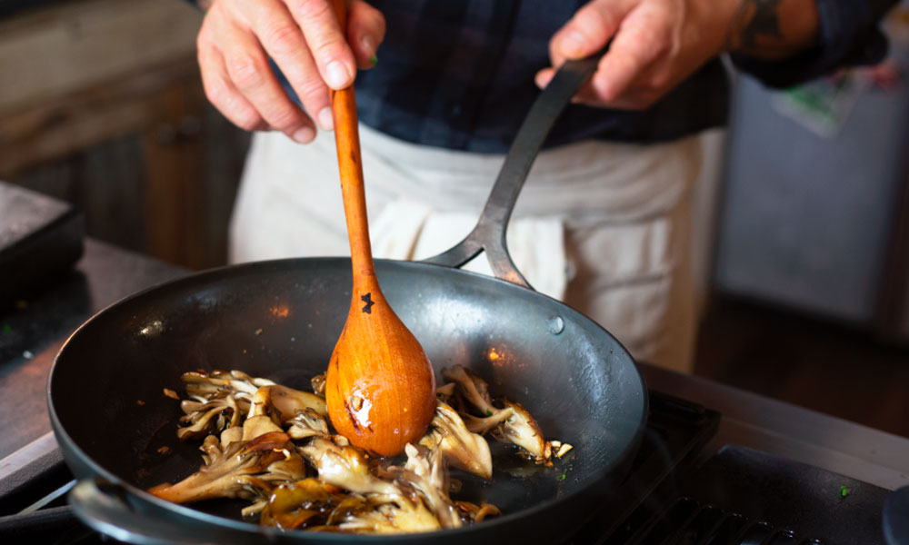 A person stirs food in a wok pan using a wooden spoon