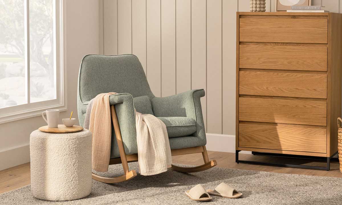 Light green rocking chair with light wooden legs and a throw blanket near a window
