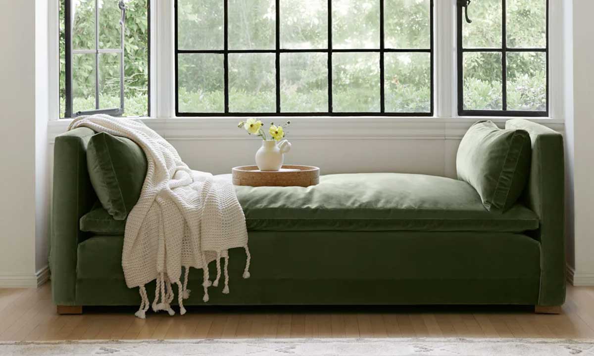 Green velvet chaise lounge with a beige throw blanket near windows in a cozy spot
