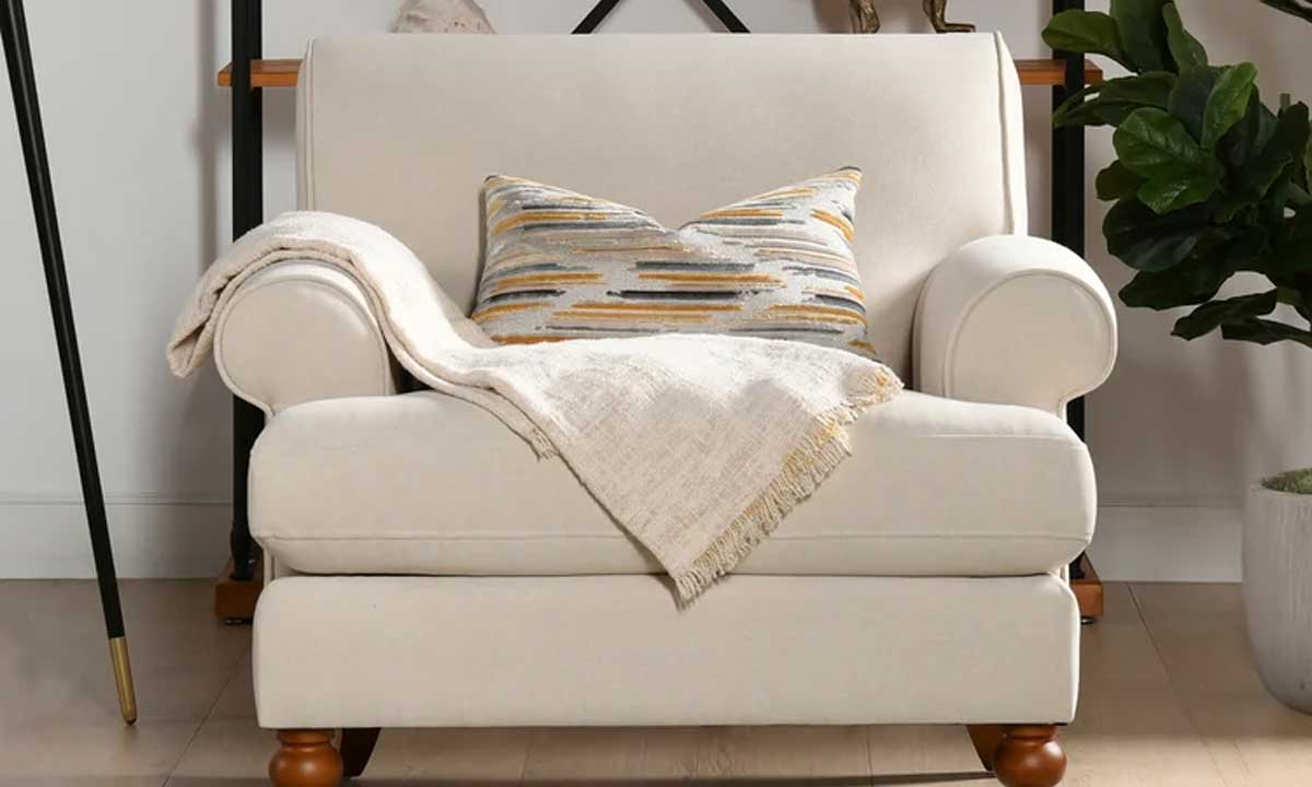 A beige english rolled armchair with a textured pillow and a throw blanket