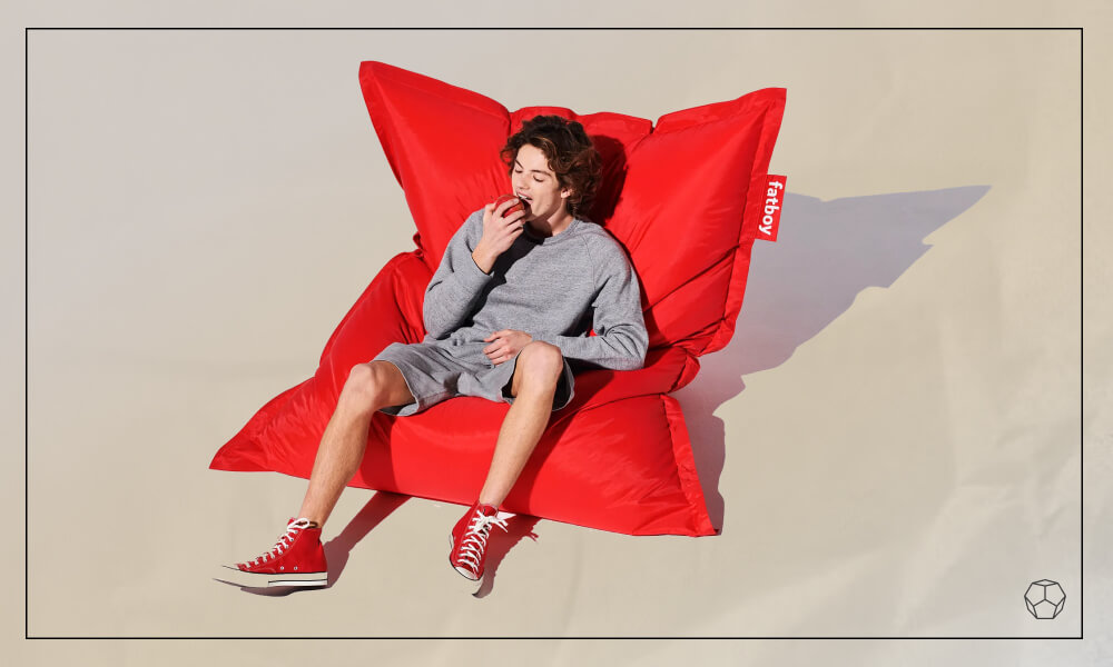 Young man sitting in a red bean bag chair eating an apple