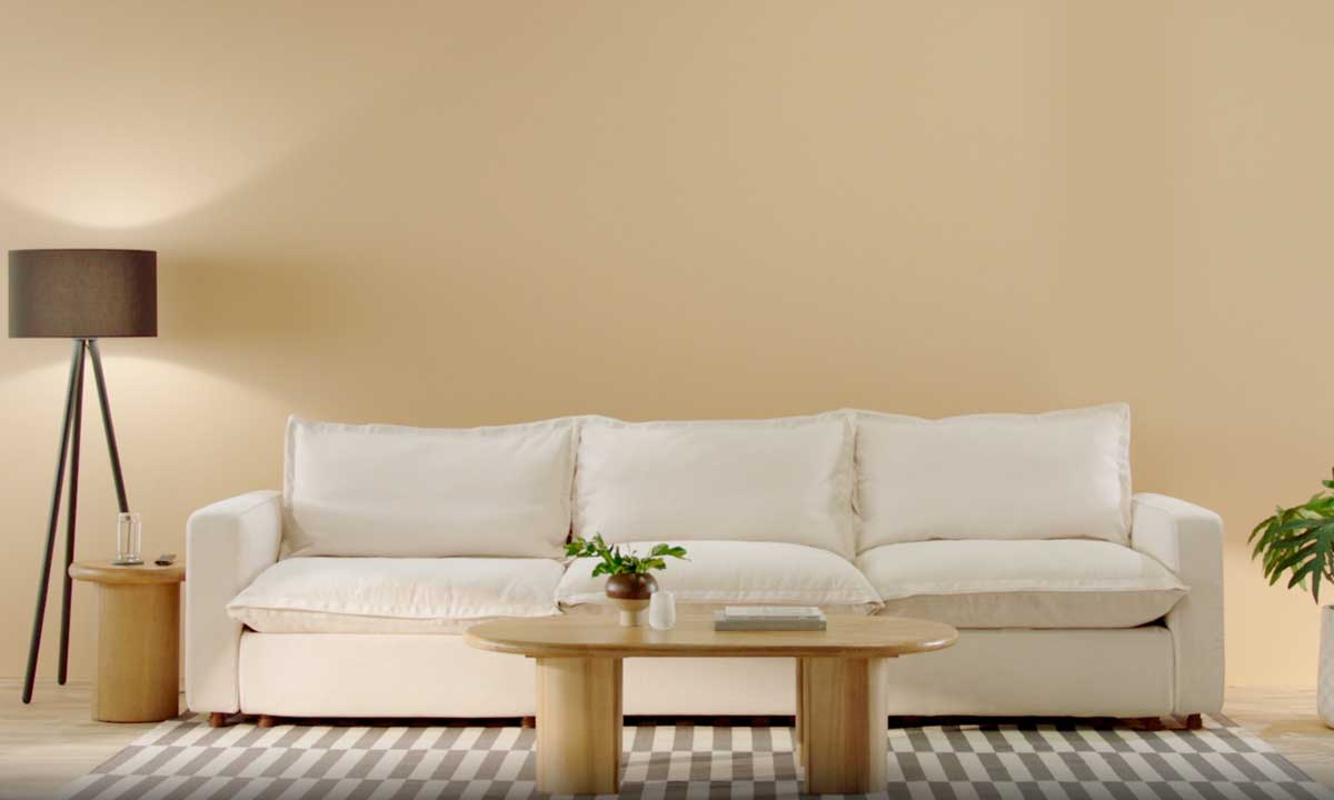 three seater white upholstered sofa in a beige room with a light wooden coffee table with a plant