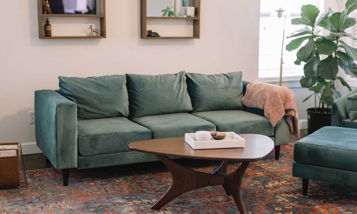 Green velvet sofa with back legs in a living room with a rug and a wooden coffee table