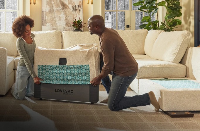 A couple is placing a cover on a section of a sofa in a living room where they are assembling it.