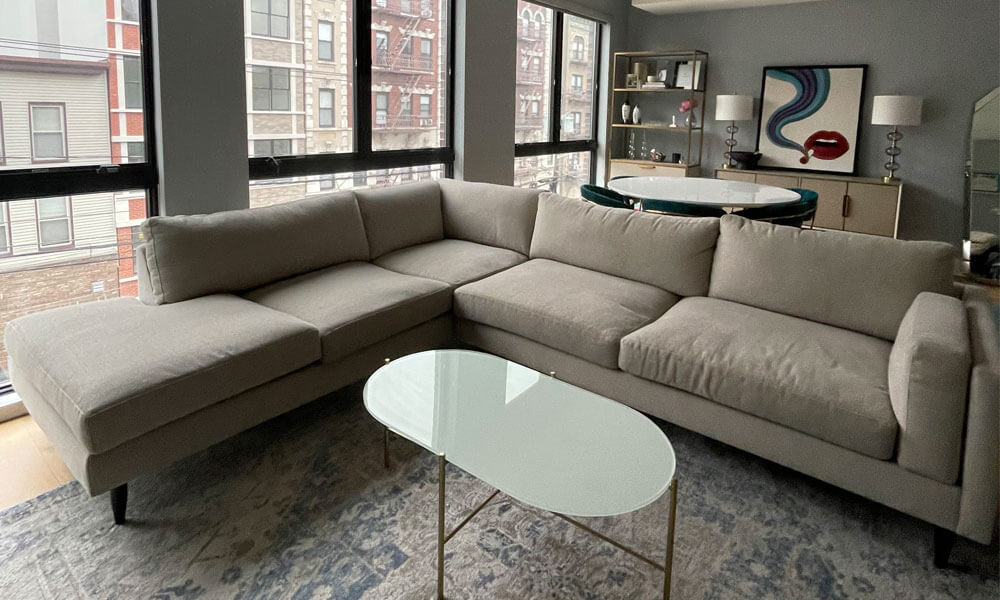 L-shaped grey upholsterd sofa in a grey living room with an oval coffee table and a boho rug