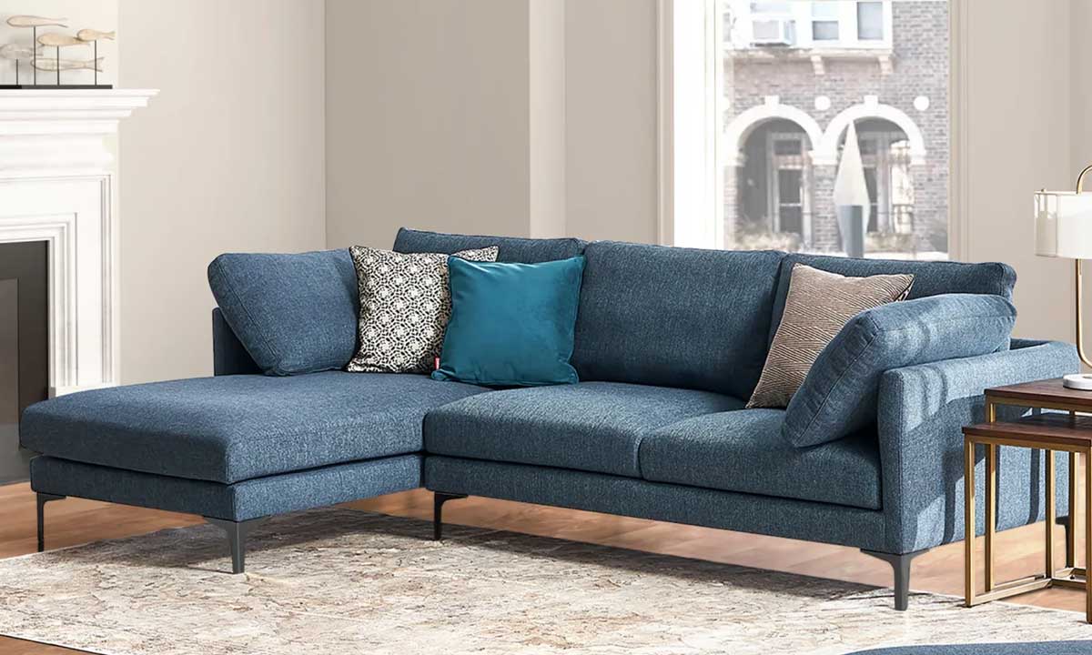 L-shaped blue upholsterd sofa with patterned throw pillows and a faded carpet in a living room