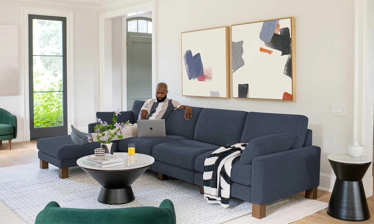 a man seated on a blue upholstered sofa in a living room, surrounded by warm decor and soft lighting