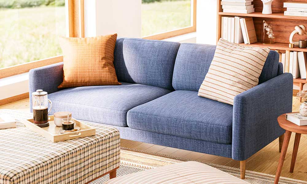 Blue upholstered sofa with orange throw pillows in living room with an ottoman coffee table