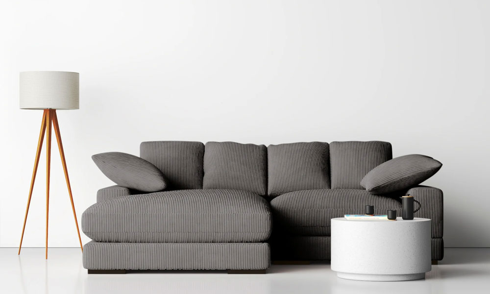 Grey upholstered low sectional sofa with two matching throw pillows, near a coffee table and a lamp