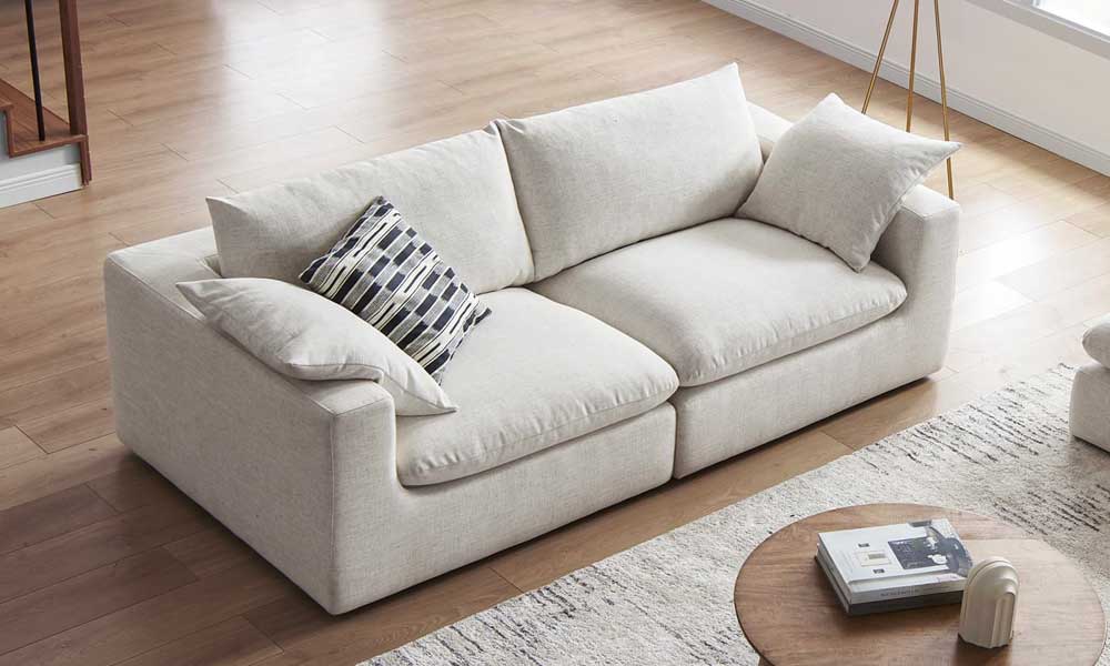 light grey upholstered low sofa with large throw pillows in a living room with coffee table and rug