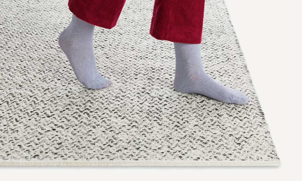 White and grey weave rug and a woman walking on it with socks
