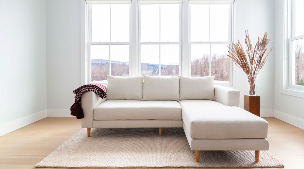 Pearl upholstered Sectional sofa with wooden legs and a red and white stripped blanket