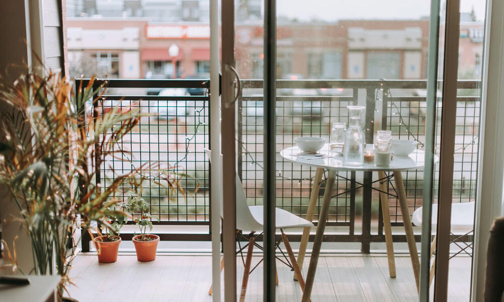 A balcony with white table and chairs near pots with plants