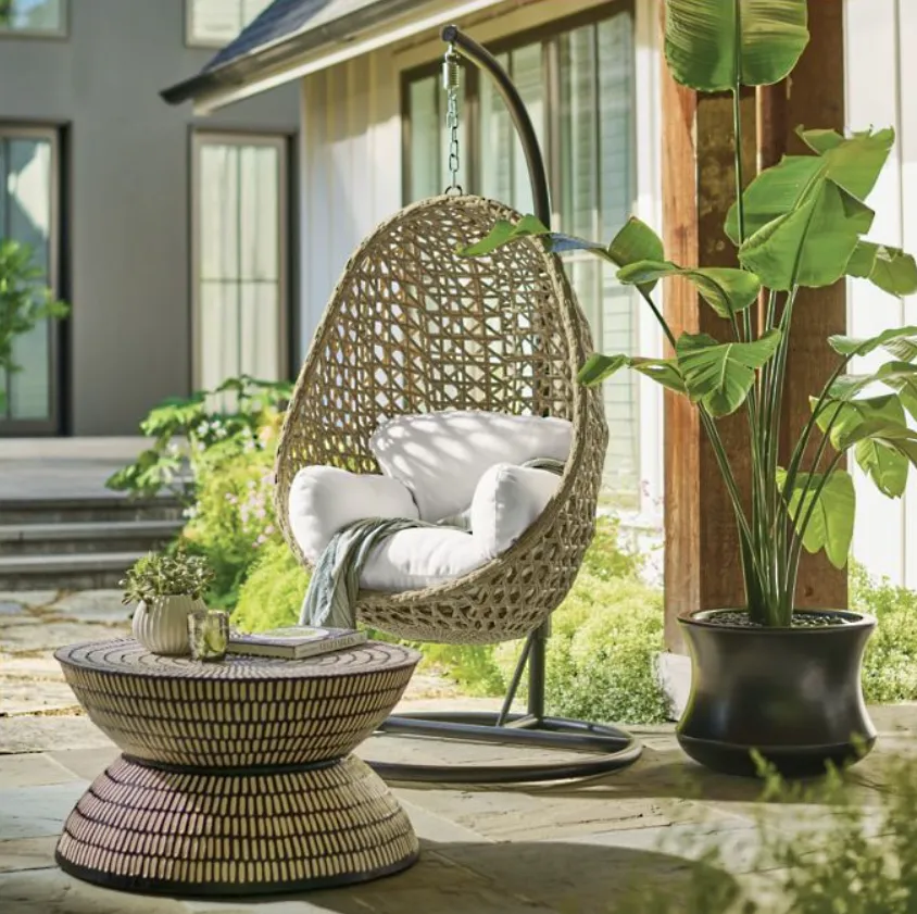Hanging wicker chair hanging from a black aluminum base in a porch near plants