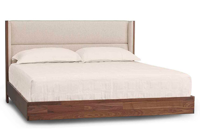 Wooden floating platform bed with a mattress and beige bedding sheets and pillows