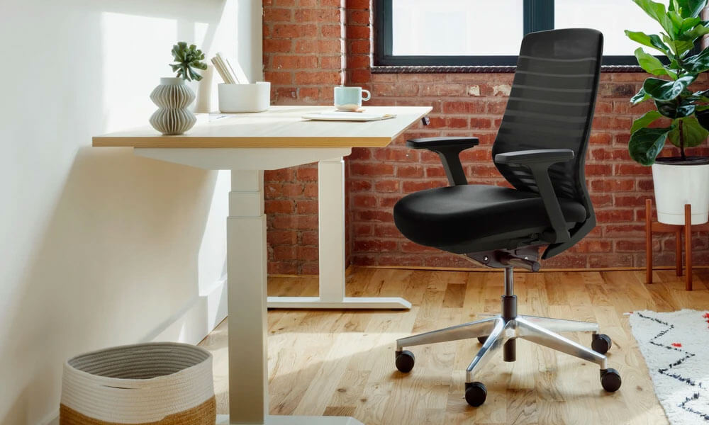 Black egonomic chair near a white framed desk with a wooden top in a home office setup