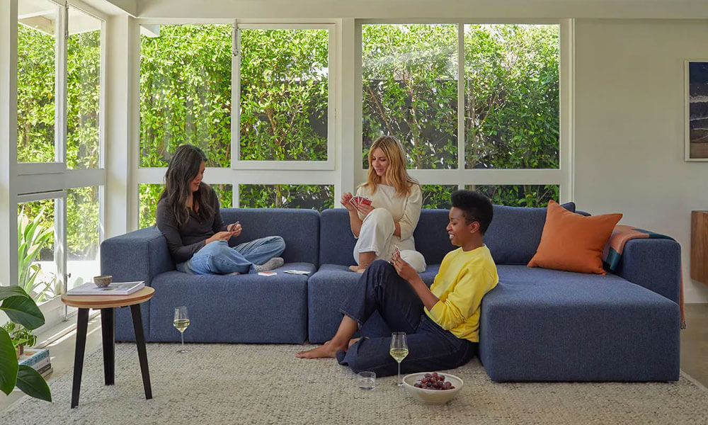 Thre women playing uno in a living room with a sectional sofa, a rug and wine cups