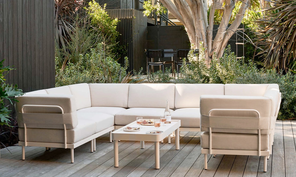 Beige outdoor Sectional with a beige coffee table in a patio near plants in a sunny day