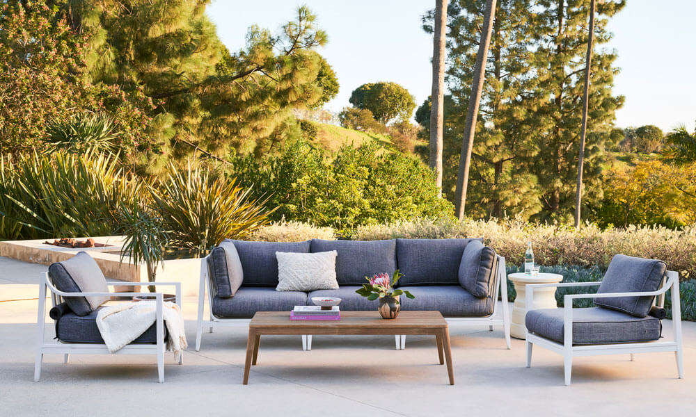 White Aluminum sofa set with dark grey cushions and a wooden coffee table outdoors near plants