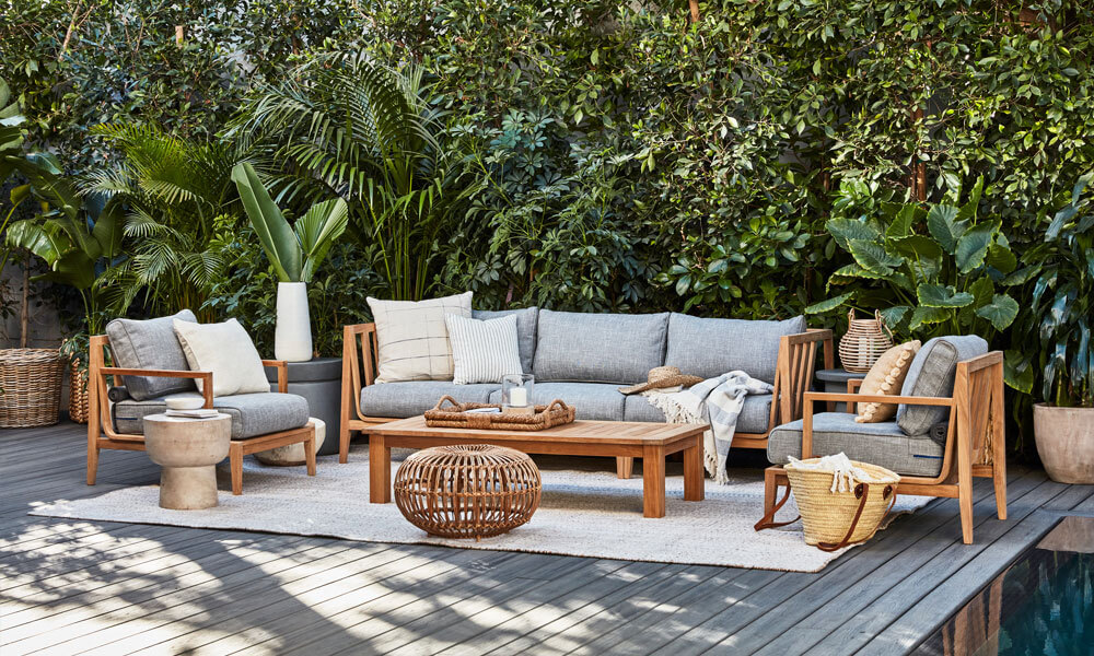 Teak Sectional with light grey cushions in a patio near a green wall and a teak coffee table