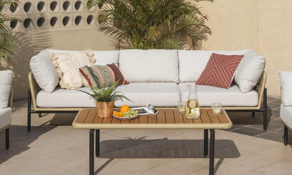 White sofa and two chairs on a patio, surrounded by lush green plants.