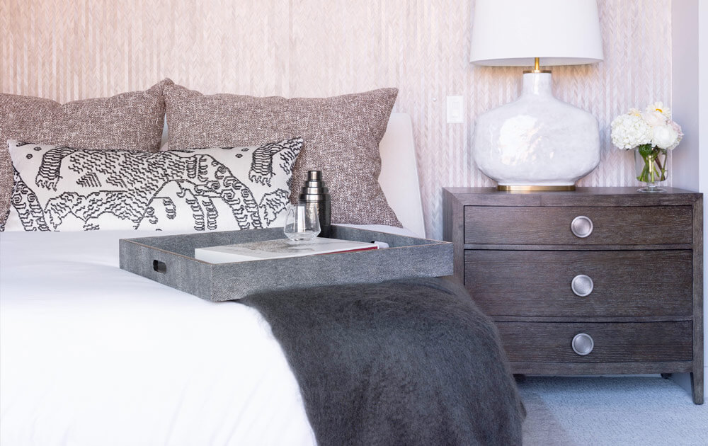 Nightstand in one side of a bed with three pillows and a modern tray