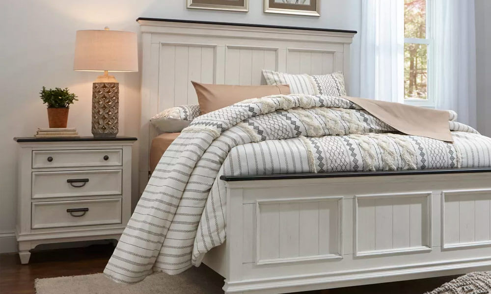 White Nightstand with a lamp and a pot with a plant in one side of a white framed bed