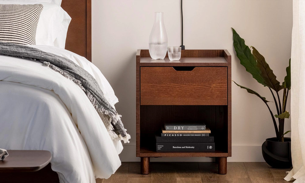 Dark wooden nightstand with one drawer on one side of a bed