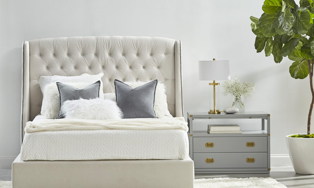 White upholstered bedframe with a gray nighstsand with two drawers in one side