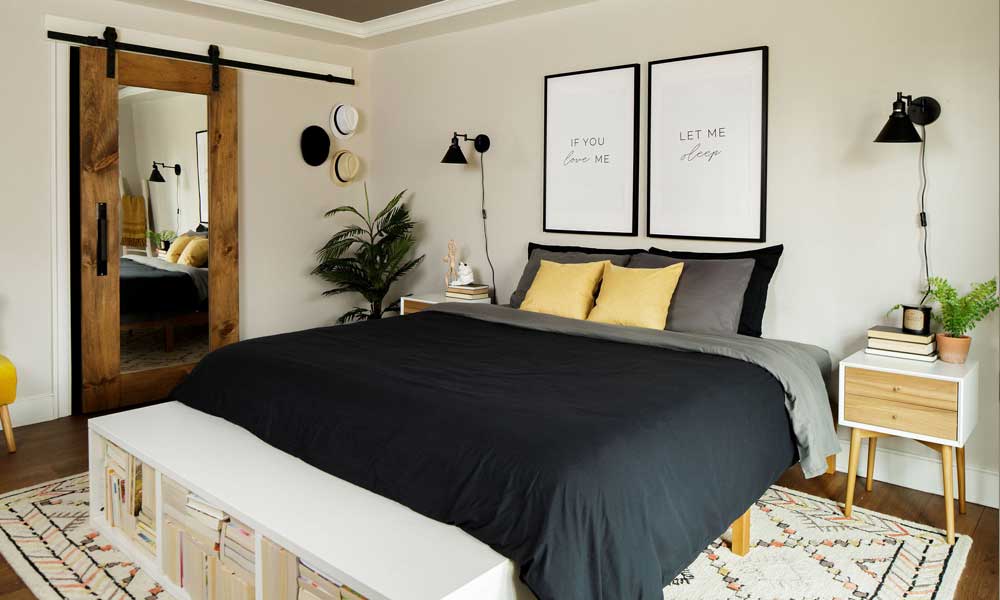 Modern Bedroom furniture with black bedding, wooden furniture, plants and a beige rug