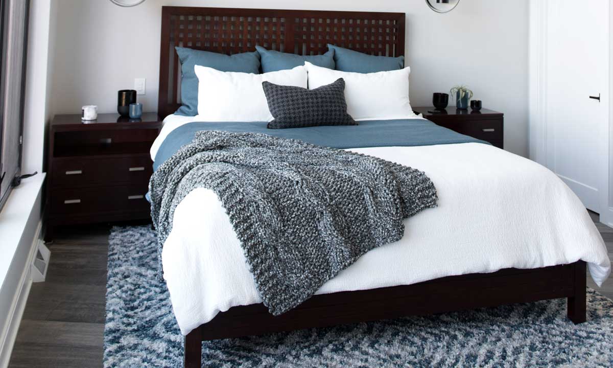 Grey Rug Under a queen size bed with a duvet and a woven blanket