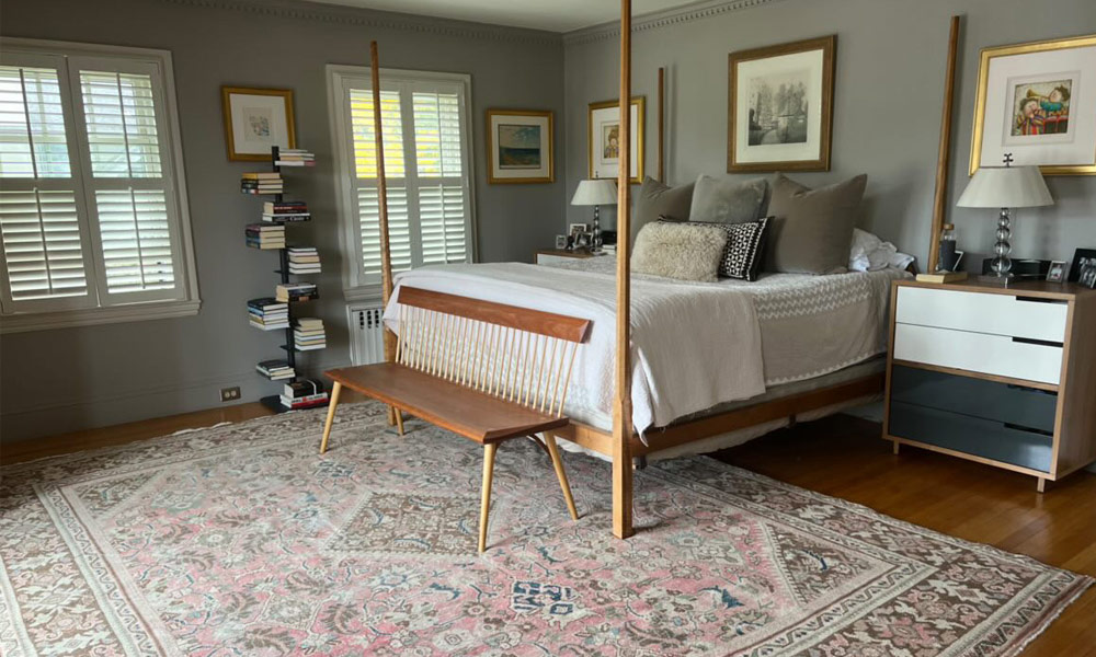 Rug under bottom third of a wooden bedframe in a cozy room with a book shelve
