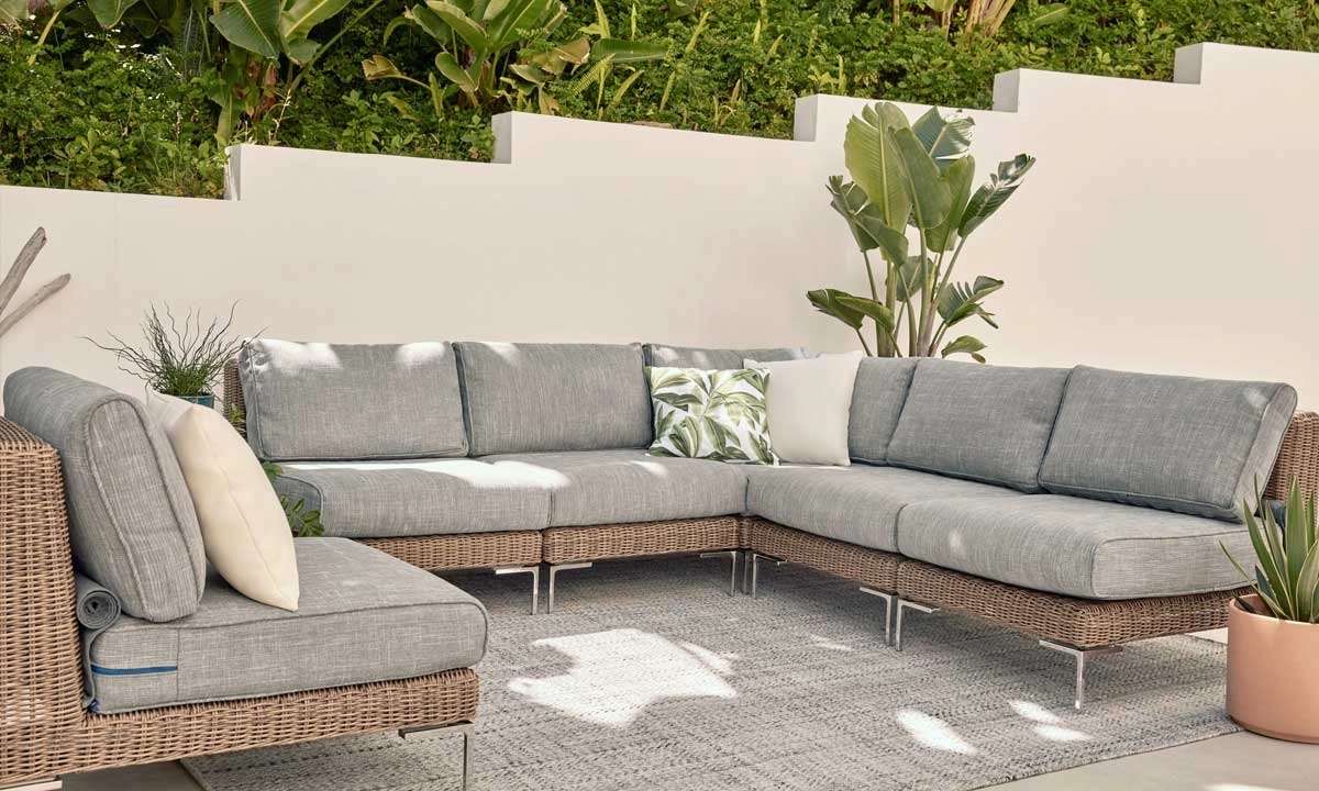 A modern outdoor sectional sofa with light gray cushions on patio with lush green plants