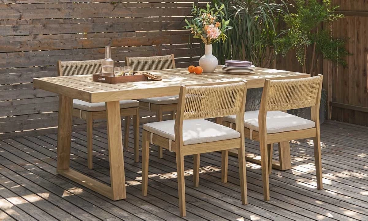 Wooden dining table with matching chairs on an outdoor patio set with plates and a vase of flowers