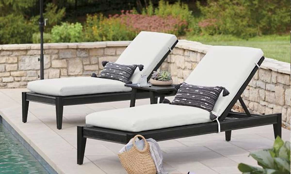 Two lounge chairs with white cushions and stripped pillows positioned by a poolside