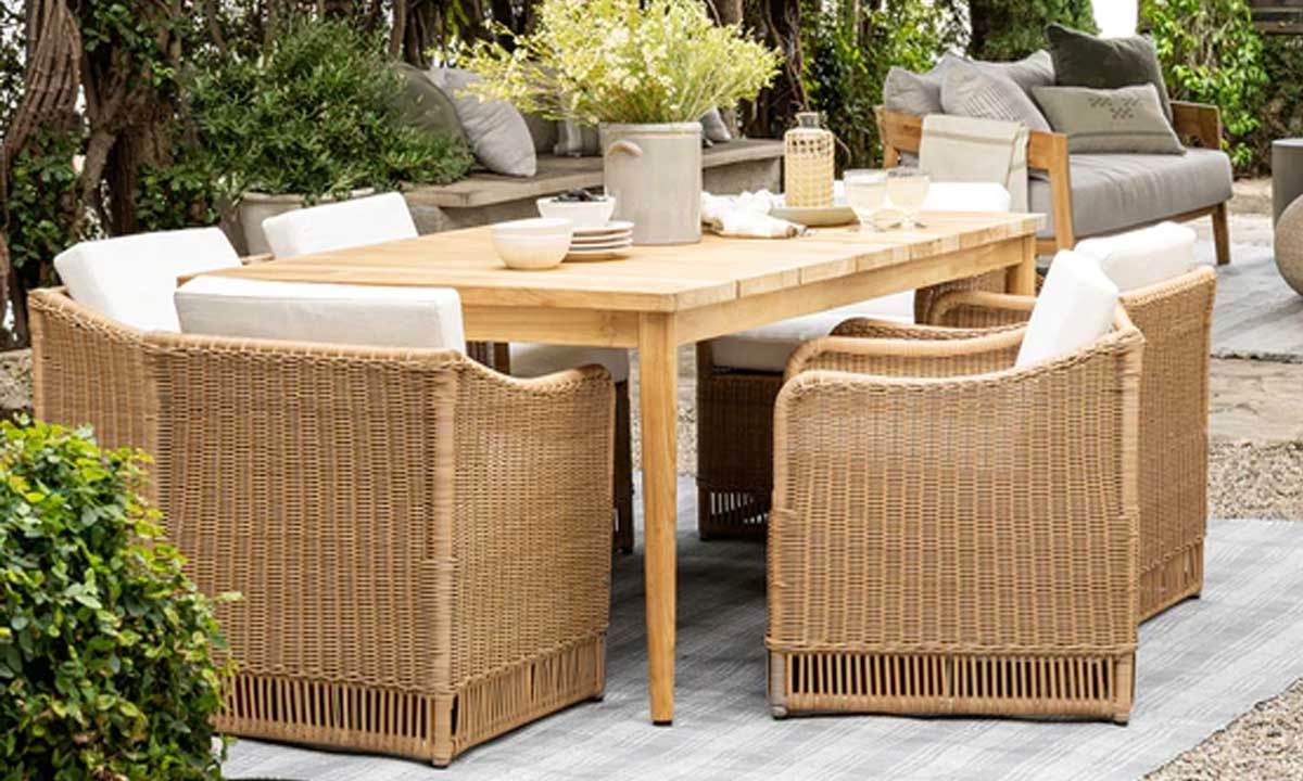 outdoor dining area with a wooden table and wicker chairs on a gravel floor