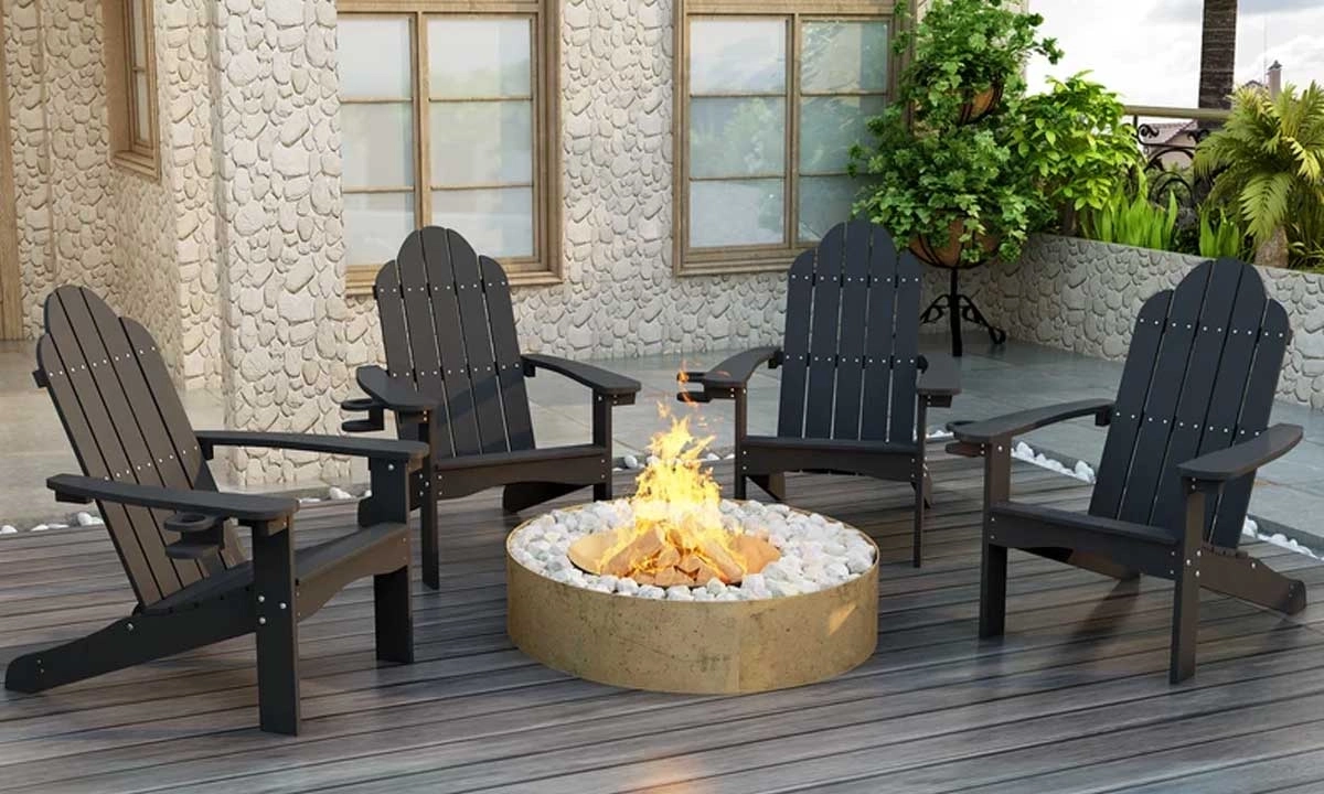 An outdoor patio setup with four dark grey adirondack chairs around a gas fire pit