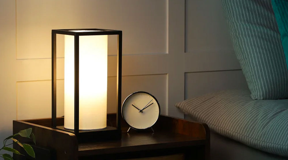 Candle shaped Table Lamp with black aluminum frame near a Bed