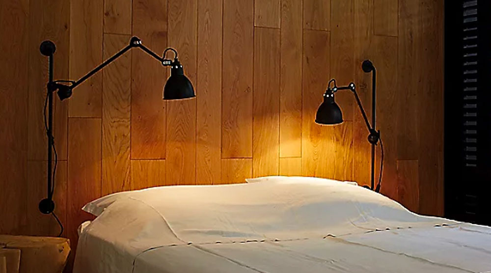 Two Swing Arm Wall Lamps in a wooden wall near a white bed with white pillows