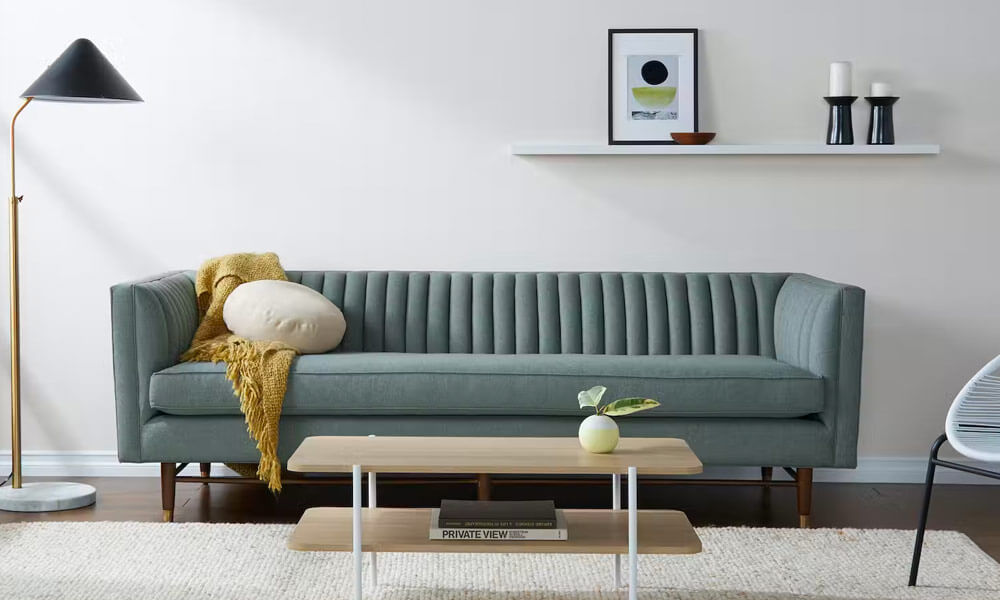 Grey upholstered Velvet Sofa with a modern design, a yellow throw blanket and a white throw pillow