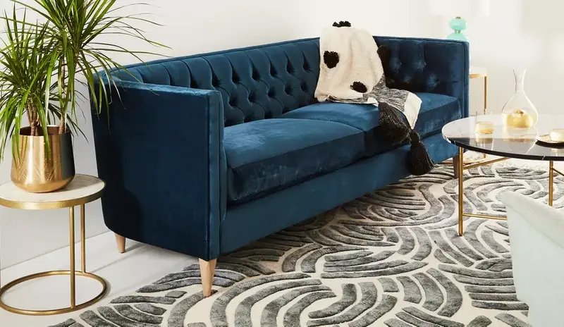 blue velvet upholstered sofa with wooden legs in a modern living space with golden decor
