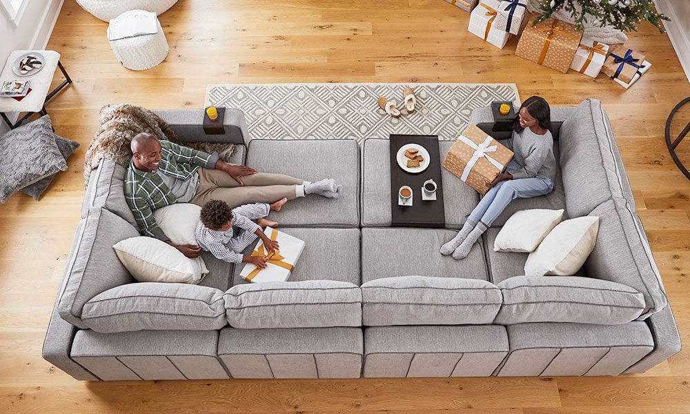 8-piece pit sectional sofa with grey upholstery. A family is sitting in it in a wooden floor living