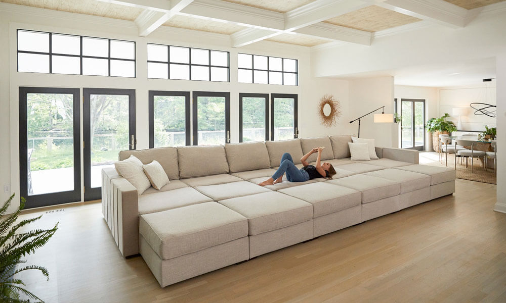 18-piece beige pit sectional sofa with a woman resting in it in a spacious living room