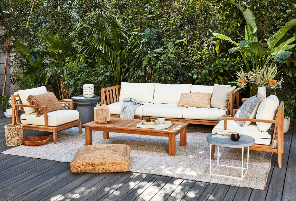Teak outdoor sofa with white cushions, a teak coffee table on a patio in a sunny day