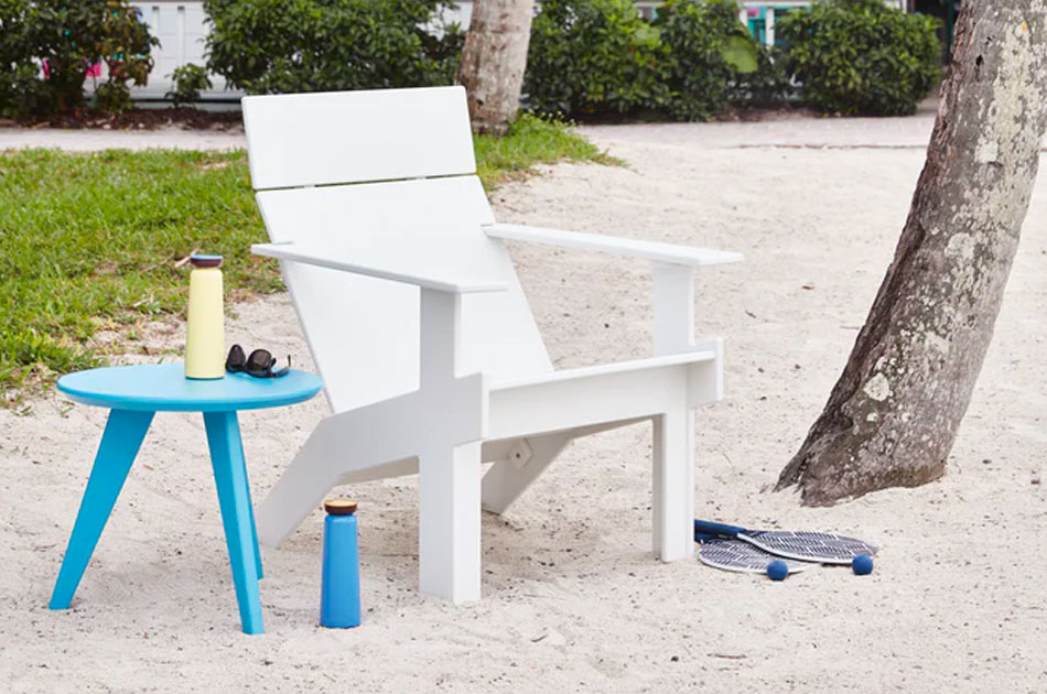 White adirondack chair with a light blue coffee table in the sand near a palm tree