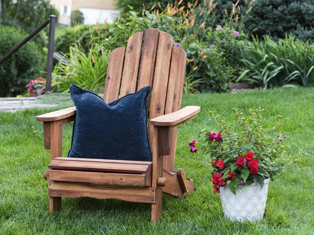 Wood Folding Adirondack Chair with a blue cushion and a pot with flowers in a garden